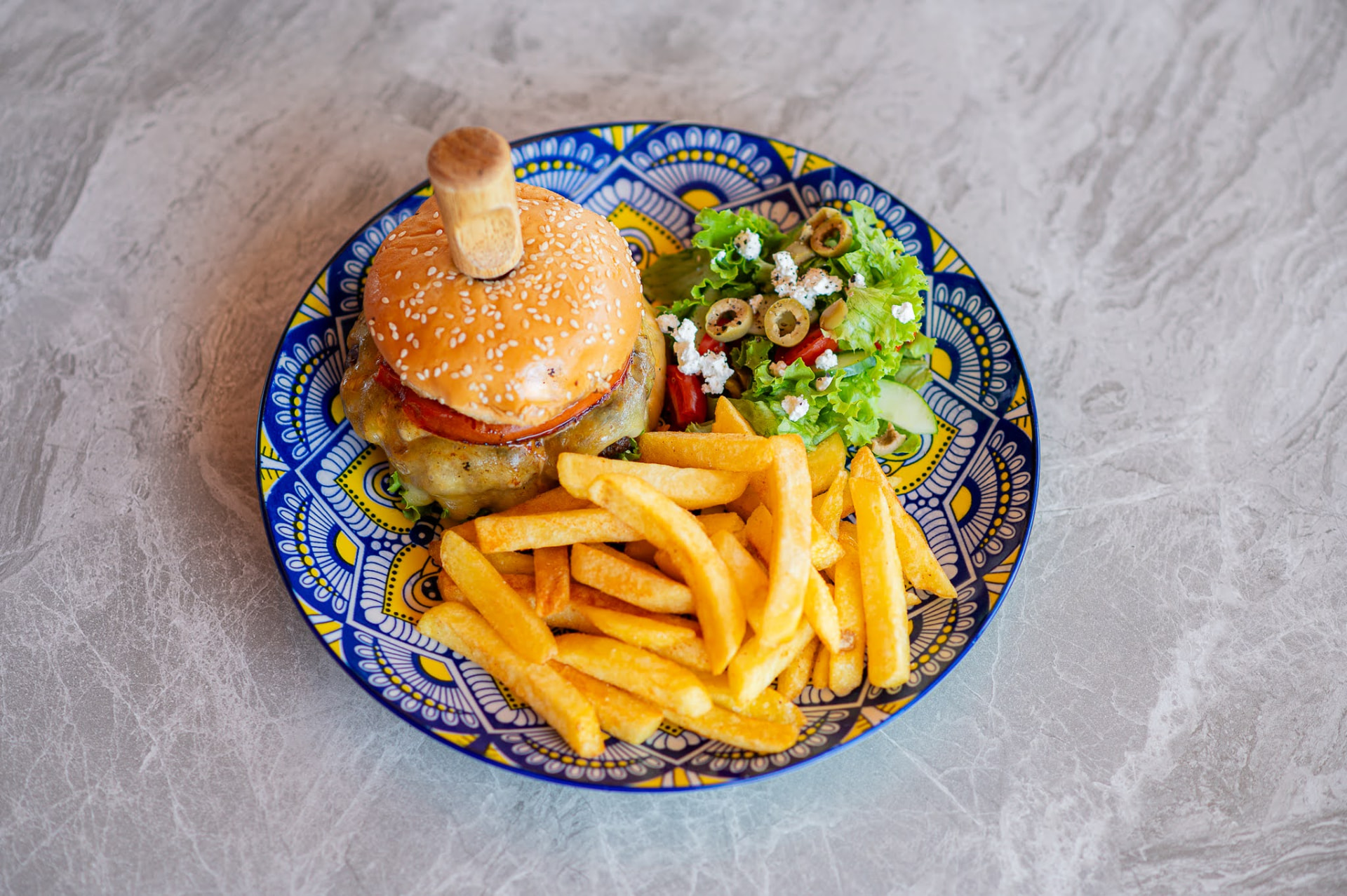 Kiwi gourmet burger with chips and Greek side salad on a hand-painted plate